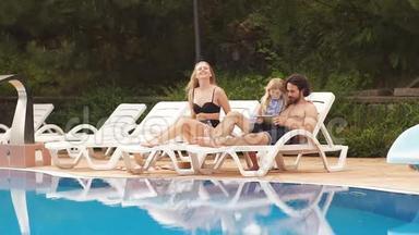 婴儿和父母在度假村游泳池附近的日光浴中放松。 时尚女孩，情侣，度假村家庭